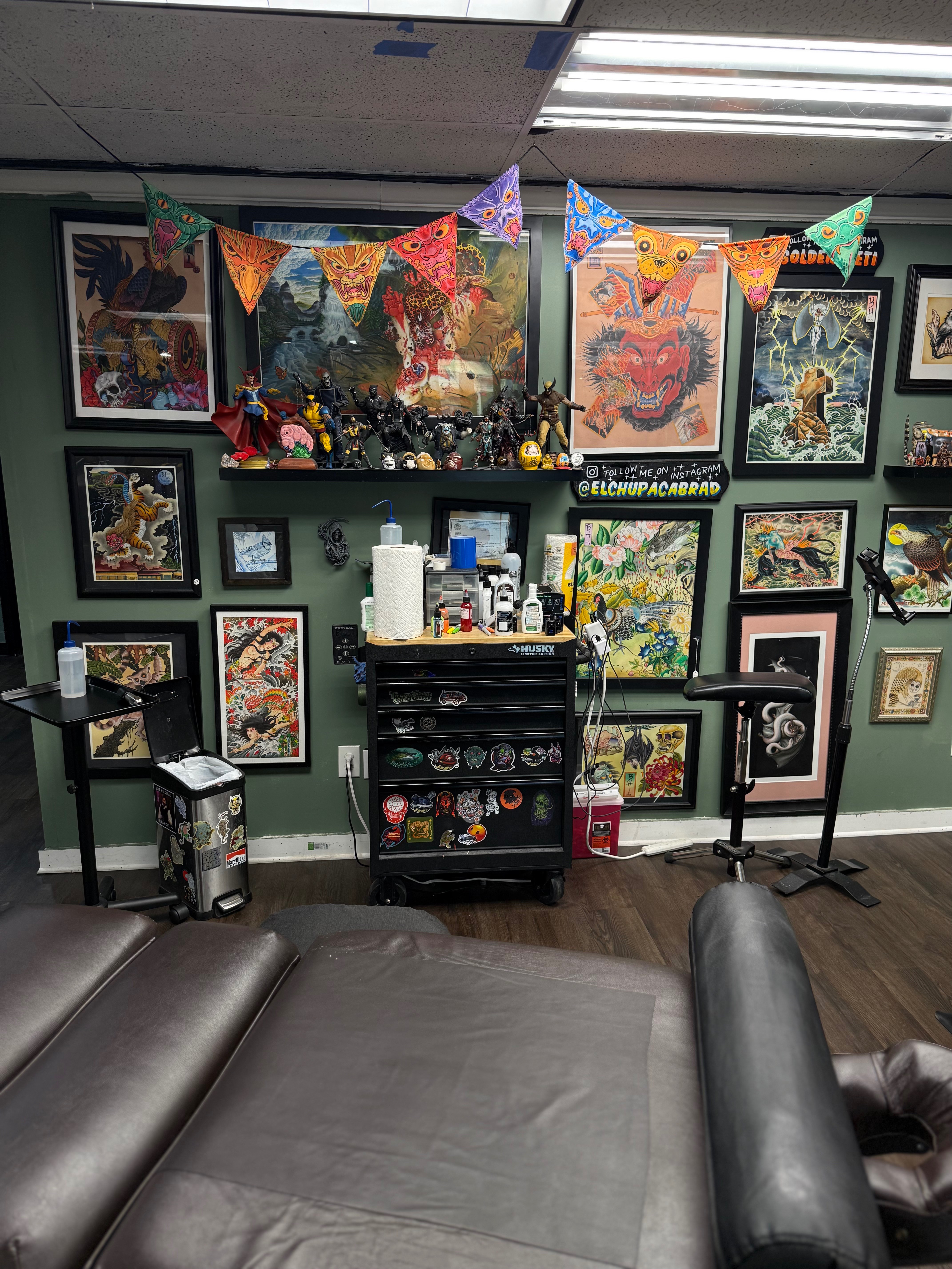 Framed art wall hung with a colorful demon-mask banner above an artist station